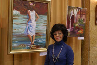 Rocío, monitora del taller de pintura, junto a dos obras en la exposición