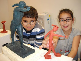 Una niña y un niño muestran sonrientes la figura que han moldeado en el taller