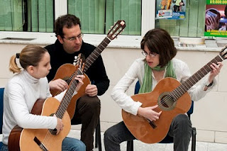 Imagen de dos de las niñas, junto a su profesor, que interpretaron el himno de Andalucía con la guitarra