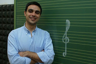 Carlos Barragán, feliz, apoyado sobre una pizarra con pentagramas en la que aparece la clave de sol