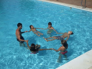 Jóvenes disfrutando del agua de la piscina, unidos de la mano, con su monitor
