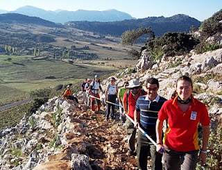 Momento de la ascensión de los marchistas por un empinado cerro. Al fondo de la imagen una espectacular vista del parque natural
