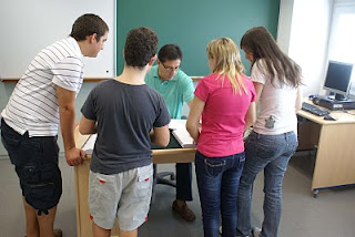 Varios alumnos acuden a la mesa del profesor para una explicación en clase de matemáticas