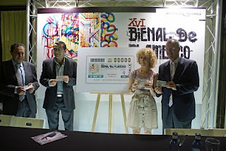 La delegada de cultura del ayuntamiento de Sevilla de pie junto al delegado territorial de la ONCE en Andalucía y el director de la Bienal posan para las cámaras con el cupón de la Bienal en la mano