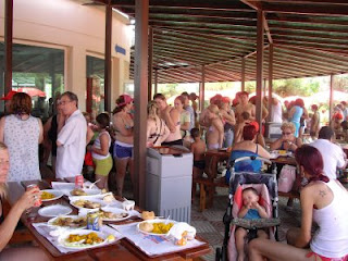 Los participantes, todos en bañador, aguardan la fila para entrar a comer