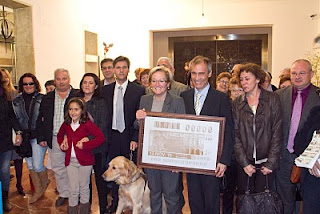 Foto de familia con todos los asitentes al acto. En el centro, mostrando sonrientes la imagen de la plancha que ha dado origen al cupón, Petronila Guerrero y Antonio Casado