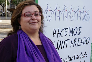 Rostro sonriente de Dolores Rivero junto a un cartel del voluntariado