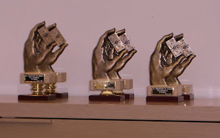 Imagen de los trofeos entregados, una mano en bronce que sostiene una ficha de dominó