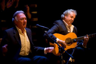 Curro Andrés cantando con expresión grave y brazos abiertos, a su derecha el guitarrista toca con ojos cerrados