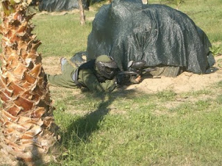 Un participante de paintball, ataviado con el traje reglamentario y su pistola de pintura, tumbado en el suelo a la espera de realizar un disparo con éxito