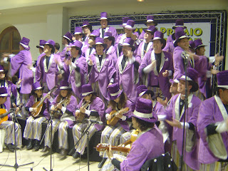 Coro de los Ilusionistas, todos de morado con sombreros altos
