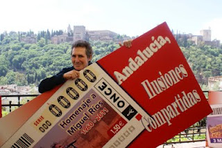 Miguel Ríos posa feliz junto a un cartel en el que aparece la imagen del cupón y el eslógan 'Andalucía, ilusiones compartidas'