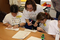 Dos alumnas entregas a los trabajos de los talleres luciendo camisetas con el abecedario braille