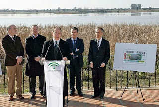 El consejero de Medio Ambiente de la Junta de Andalucía, Juan José Díaz Trillo, durante su intervención en la presentación del cupón. Tras él, el delegado de la ONCE en Andalucía, Patricio Cárceles, el director de la ONCE en Huelva, Antonio Casado, el alcalde de Almonte, Francisco Bella y el director del espacio natural de Doñana, Juan Carlos Rubio con la plancha del cupón a la derecha de la imagen y al fondo las marismas de Doñana
