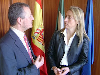 El delegado territorial de la ONCE y la directora general de Juego hablan junto a las banderas de Andalucía, España y la Unión Europea