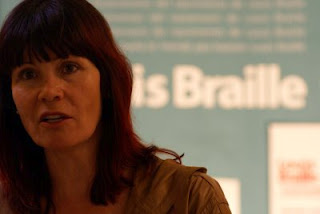 Primer plano del rostro de Micaela Navarro con el cartel braille al fondo