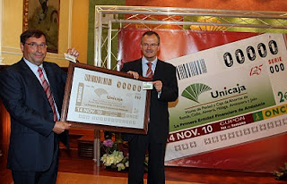 El delegado de la ONCE y el secretario general de Unicaja muestran a las cámaras la imagen del cupón