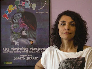 Loreto Suárez sonriente junto a un cartel de su Agrupación Las Cacatúas Parlantes