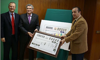 El consejero de Gobernación, el director de la Agencia Andaluza para el Voluntariado y el delegado territorial de la ONCE muestran el cupón dedicado al voluntariado