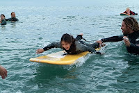 Una niña feliz tumbada sobre la tabla ya en el agua recibiendo las instrucciones de su monitor
