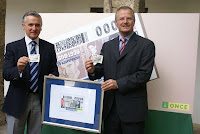 El consejero de Cultura de la Junta de Andalucía, Paulino Plata, junto al delegado de la ONCE en Andalucía, Ceuta y Melilla, Patricio Cárceles, posando con un ejemplar del cupón dedicado a Lorca y el cartel con la imagen del cupón.