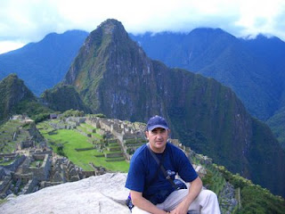 Pepe Perea agachado con una espectacular vista de la ciudad perdida de Machu Picchu al fondo