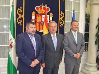 El delegado territorial y el presidente del Consejo posan con el delegado del Gobierno frente a un tapiz y las banderas de España y Andalucía