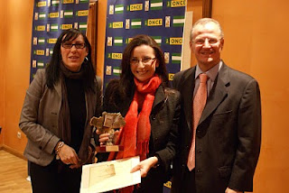 La ganadora del Premio al mejor Relato Corto, Silvia Ortega, posa sonriente mostrando su galardón, junto a Mónica Madrid, a su derecha, y Patricio Cárceles, a su izquierda