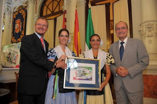 Cárceles y de la Torre posan con una imagen de la copia del cupón y con el grupo folclórico que aparece en el mismo