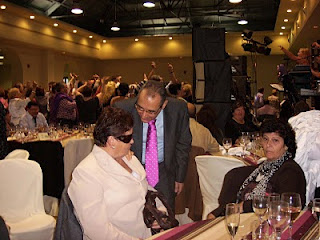 El director de la ONCE en Cádiz, Francisco Arroyo, hablando con una afiliada y de fondo un grupo bailando al ritmo de la música