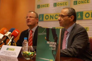 En primer plano, un ejemplar de la Memoria ONCE 2010 y tras él, el delegado territorial, Patricio Cárceles, y el subdelegado, Francisco Arroyo, durante la rueda de prensa de la presentación de la Memoria'10 en Sevilla