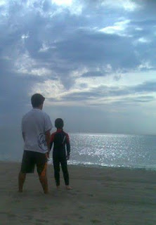 Bella estampa con el cielo nublado de dos niños frente al mar en el atardecer