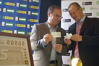 El delegado territorial de la ONCE y el presidente de la Unión de Consumidores, sonrientes, enfrascados en una distendida conversación con el cupón conmemorativo en la mano
