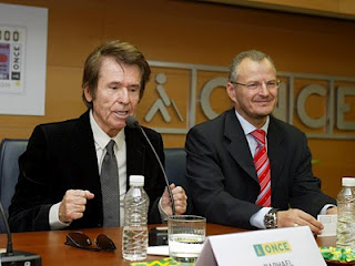 Raphael dirigiendo unas palabras al auditorio. A su lado, sonriente, Patricio Cárceles, delegado territorial de la ONCE en Andalucía