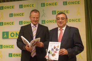 El delegado territorial ojea un ejemplar de la Memoria junto al director en Huelva con otro ejemplar de la publicación