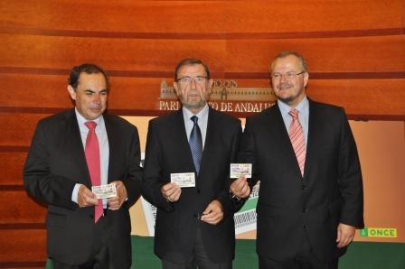 El delegado territorial de la ONCE en Andalucía, Ceuta y Melilla, Patricio Cárceles, el presidente del Consejo Territorial de la ONCE en Andalucía, Ventura Pazos, y el presidente de la Mesa del Parlamento sostienen el cupón conmemorativo