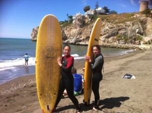 En la imagen, dos niñas posan junto a su tabla de surf