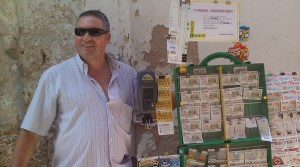 En la imagen, el vendedor Francisco Amador posa junto a su stand de cupones situado en el barrio de La Viña