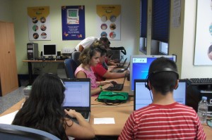 En la imagen, 6 alumnos ante sus ordenadores practican lo aprendido en el curso mentras dos profesores les explican la lección