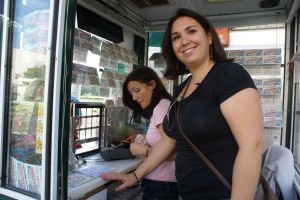 En la imagen, María Díaz, administrativa de Alentis, durante su jornada en el quiosco de Mª José Domínguez. La trabajadora de Alentis mira a la cámara mientras la vendedora atiende a unos clientes vendiéndoles un cupón
