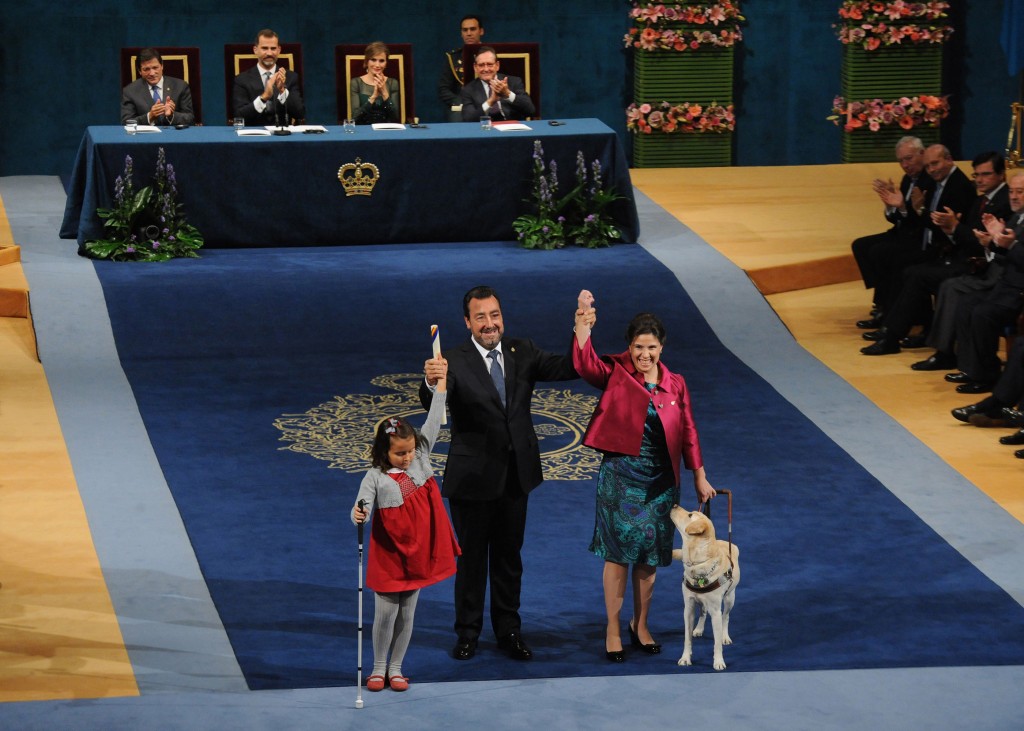 Momento histórico para la ONCE. El presidente de la ONCE y su Fundación, Miguel Carballeda, acaba de recoger el premio Príncipe de Asturias de la Concordia para la ONCE de manos de S.A.R. el príncipe don Felipe, acompañado por dos afiliadas, la niña ciega de ocho años Liv Parlee Cantin, que acautivó al auditorio del Teatro Campoamor con su simpatía, y María Cristina Lucchese, cuyo perro guía Breezy, provocó más de una mirada de ternura.