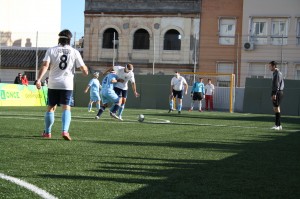 El jugador del Málaga. vestido de blanco, regatea al defensor que lo agarra de la camiseta para impedir su avance