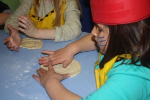 Los niños aprendieron a mezclar los ingredientes para preparar la masa de pizza Una niña extiende sobre una mesa la masa de una pizza con sus manos
