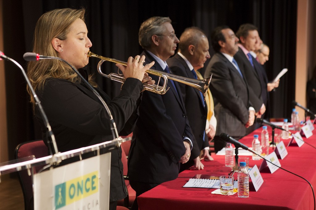 La mesa presidencial puesta en pie escucha el himno de Andalucía interpretado por la trompetista de la Sinfónica de Sevilla, Nuria Leiva