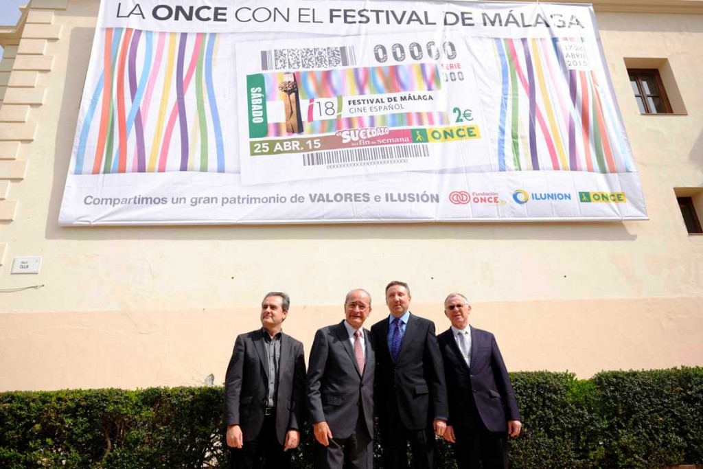 El acalde de Málaga, Francisco de la Torre, junto al director del Festival de Málaga, el delegado territorial de ONCE Andalucía, Cristóbal Martínez, y el director de la ONCE en Málaga, José Miguel Luque fernte a la pancarta del cupón conmemorativo