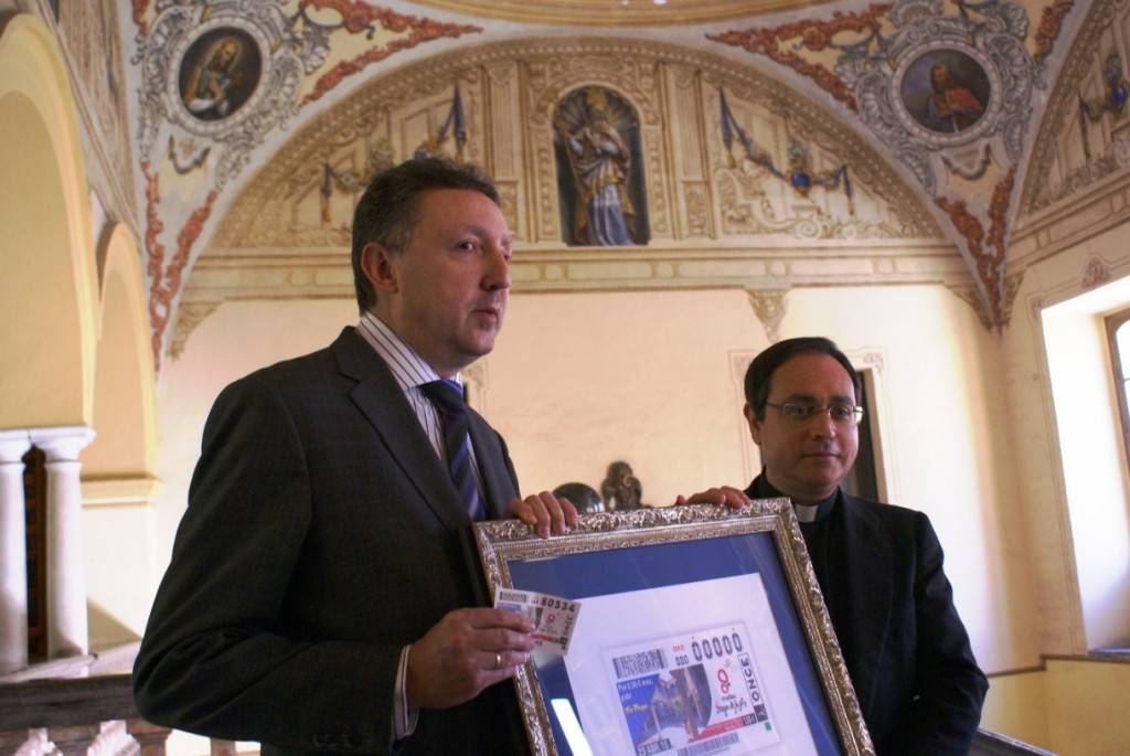 El delegado territorial de ONCE en Andalucía, Cristóbal Martínez, posa junto al vicario general de la Archidiócesis de Sevilla, Teodoro León, mientras sostienen la imagen del cupón