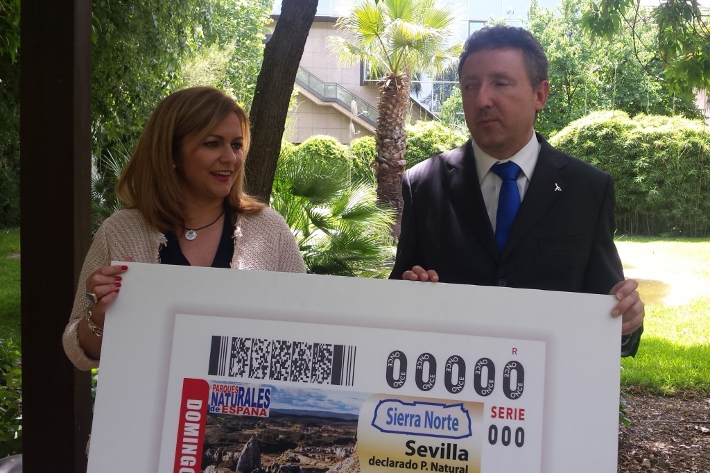 El delegado territorial de la ONCE en Andalucía, Ceuta y Melilla, Cristobal Martínez, junto a la consejera de Medio Ambiente en funciones de la Junta de Andalucía, María Jesús Serrano, sosteniendo la imagen del cupón de la Sierra Norte de Sevilla