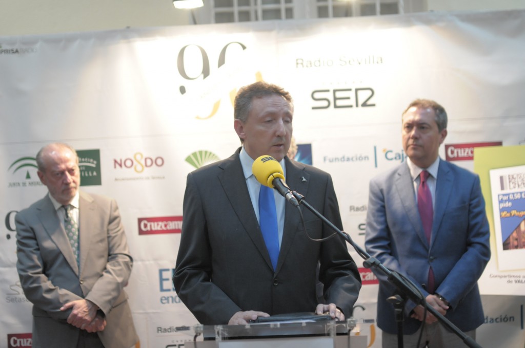 Cristóbal Martínez hablando desde el atril entre el presidente de la Diputación y el alcalde de Sevilla