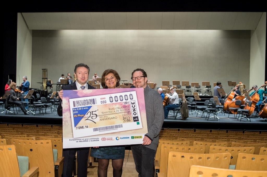 Cristóbal Martínez, delegado territorial de la ONCE en Andalucía,  Remedios Navarro, directora gerente de la ROSS y del Teatro Maestranza y John Axelrod, director artístico y musical de la ROSS. Muestran la imagen del cupón durante el acto de presentación en el Teatro Maestranza
