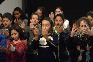Niños afiliados y no afiliados con sus manos abiertas cantando en un momento del ensayo.